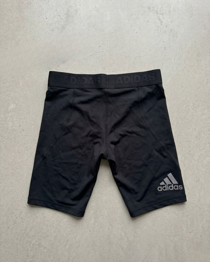 Black adidas Alphaskin compression shorts laid flat on a pale background, adidas wordmark at the hip.