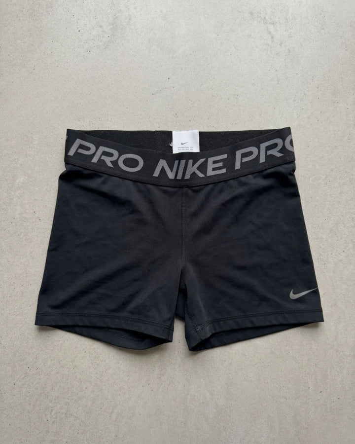 Black Nike Pro compression shorts laid flat on a pale background, NIKE PRO waistband and a small swoosh at the hem.